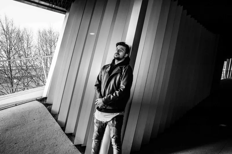 Yohann Warren leaning against angular white architectural panels in a corridor, black and white